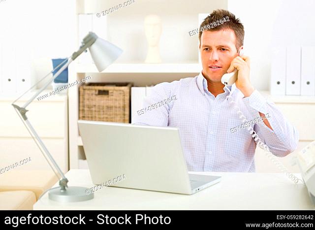 Business man working on computer at home calling on phone