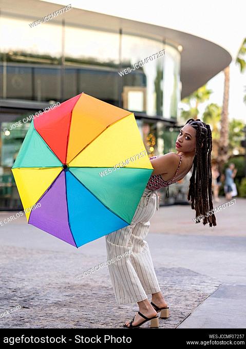 Woman holding colorful umbrella bending over backward on footpath