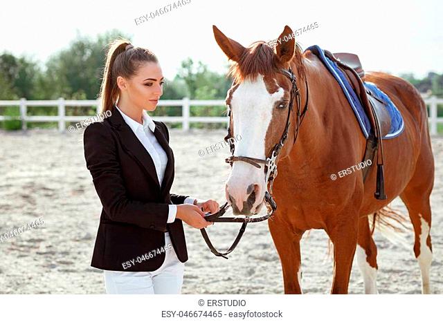 portrait of rider elegant woman with her horse outside. jockey and brown horse