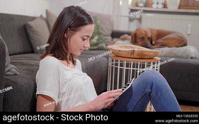 Pretty woman sits on the floor in her living room and works on her tablet computer