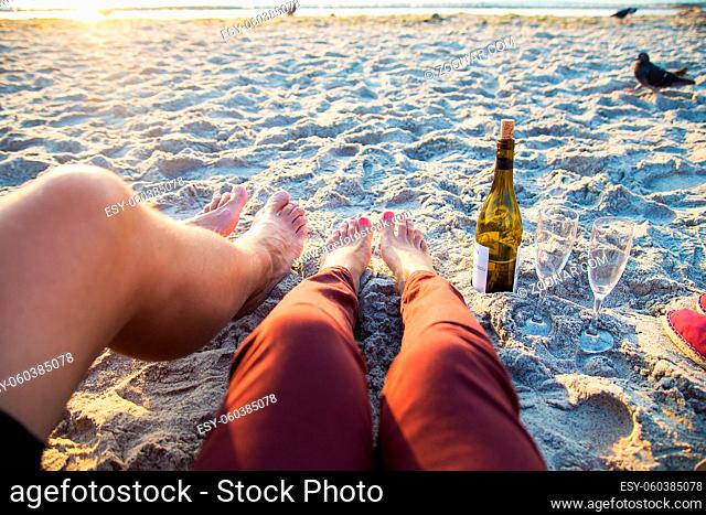 Happy stylish pair of legs on the beach sunbathing, drinking wine