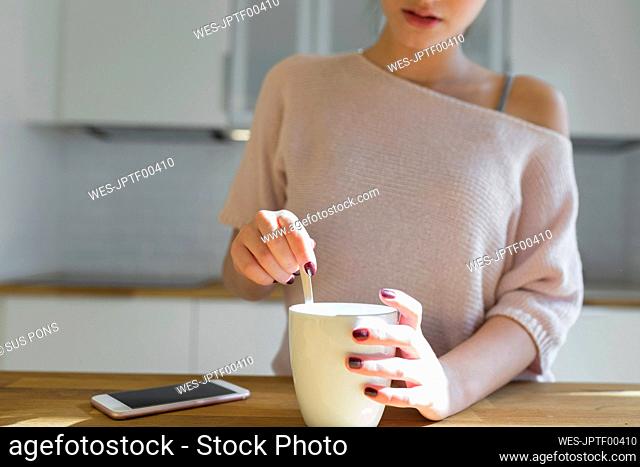 Female teenager with mug and smartphone in the kitchen