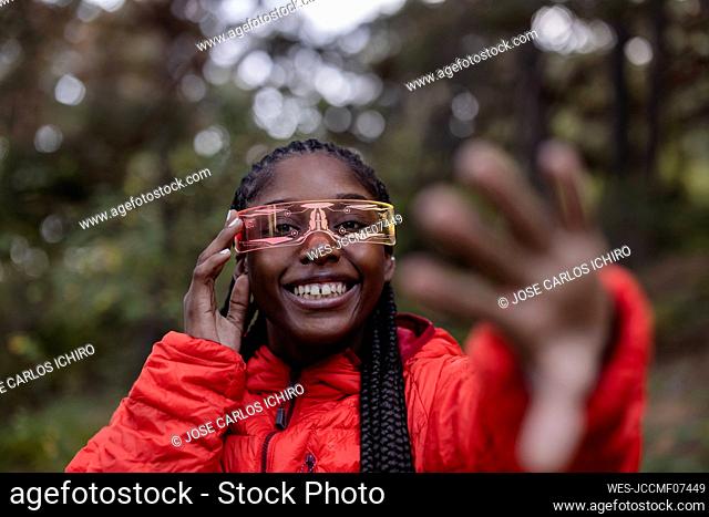 Happy young woman with futuristic glasses gesturing in forest