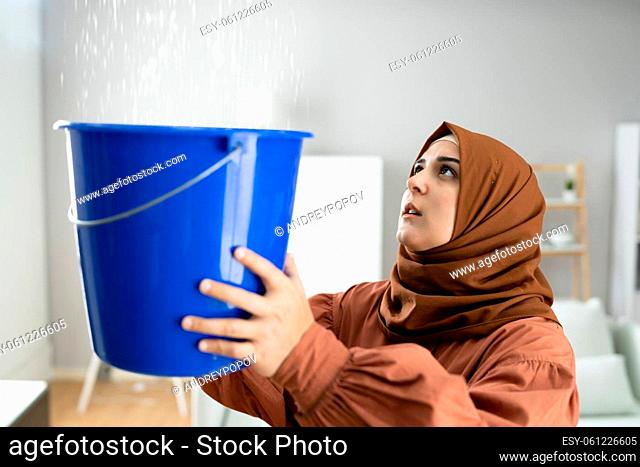 Female Worried Woman Holding Bucket While Water Droplets Leaking From Ceiling
