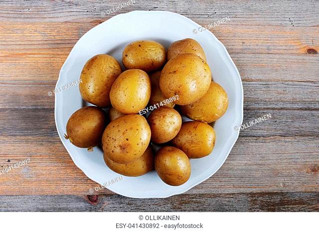 boiled potatoes in their skins on a plate, wooden background