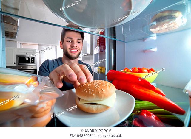 Smiling Young Man Touching The Burger In Refrigerator
