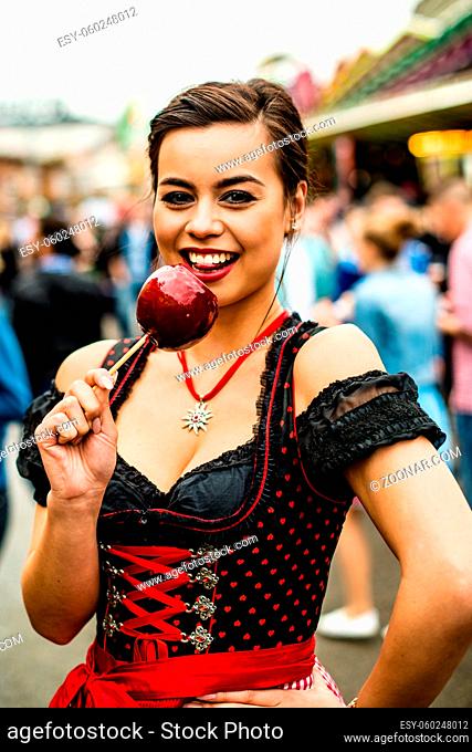 Attractive young woman holding a red caramelized apple at the Oktoberfest with people in the background