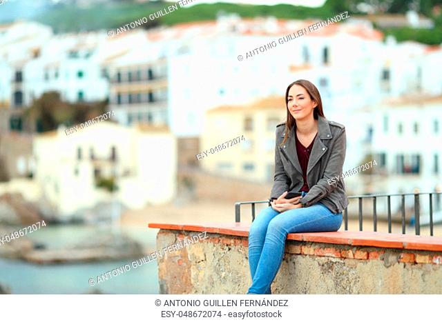 Relaxed woman contemplating ocean from a ledge in a coast town on vacation