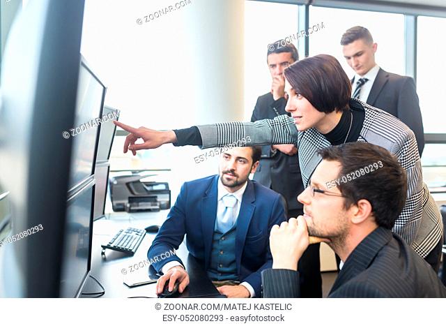 Business team looking at data on multiple computer screens in corporate office. Businesswoman pointing on screen. Business people trading online