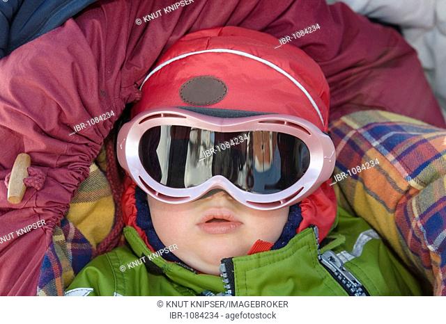 Girl, 1, wearing ski goggles lying well protected from cold weather in a buggy, Kiruna, Lappland, North Sweden, Sweden