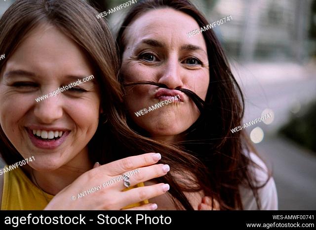 Playful woman making mustache with hair of friend