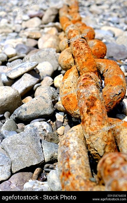 Rostige Ankerkette mit grossen Kettengliedern liegt im Kies des Rheinufers. Hochformat. Rusty anchor chain with large chain links lies in the gravel of the...