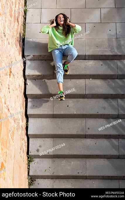 Cheerful woman enjoying music through headphones while sitting on staircase