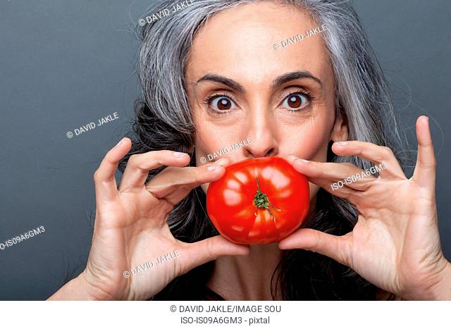 Mature woman covering mouth with red tomato