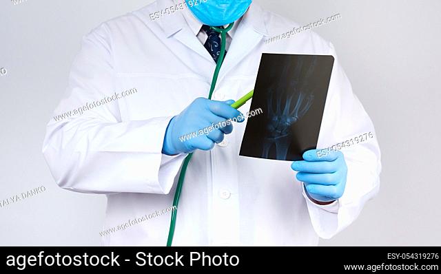 doctor in a white coat and blue latex gloves holds an x-ray of a manâ. . s hand and conducts a visual examination, white background