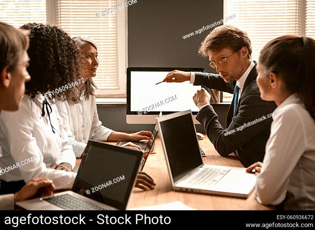 Teamwork of diverse group. Man in a business suit points to the screen. Other employees listen to a colleague. High quality photo
