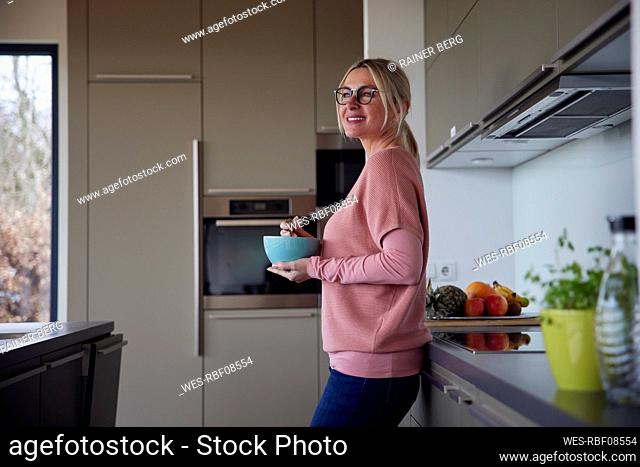Smiling blond woman with bowl standing in kitchen