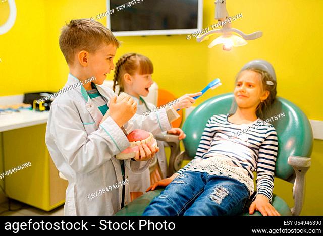 Children in uniform playing dentist doctor, playroom. Kids plays medicine worker in imaginary hospital, stomatologist profession learning, childish dream