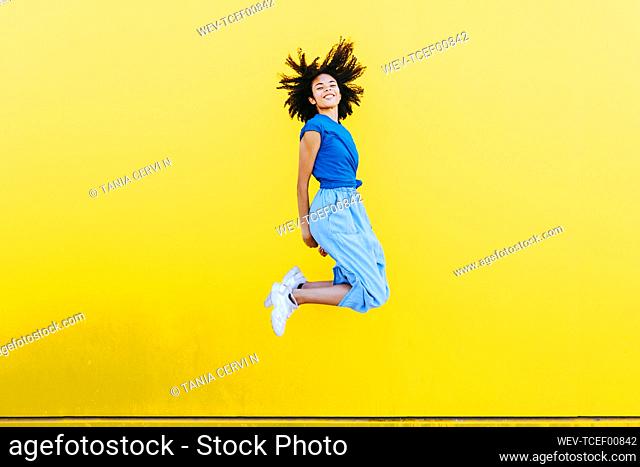 Pretty woman jumping for joy in front of yellow wall