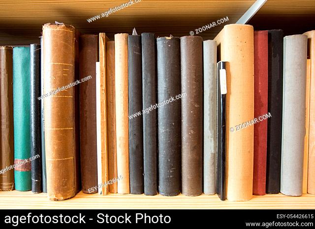 Many old dusty books in a library on a wooden shelve
