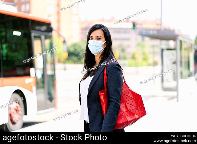 Portrait of woman wearing protective mask waiting at bus stop, Spain