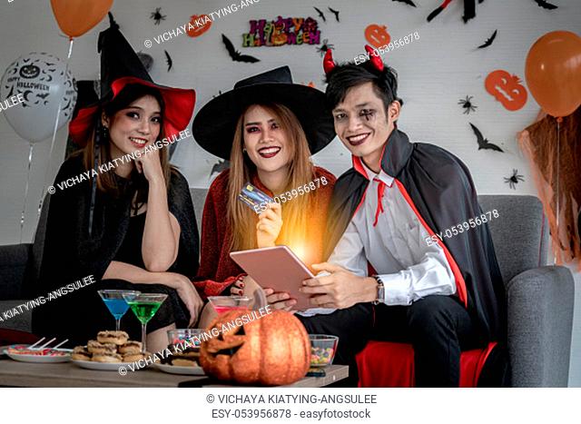 Group of young adult and teenager people celebrating a Halloween party carnival Festival in Halloween costumes and making online shopping with tablet and credit...