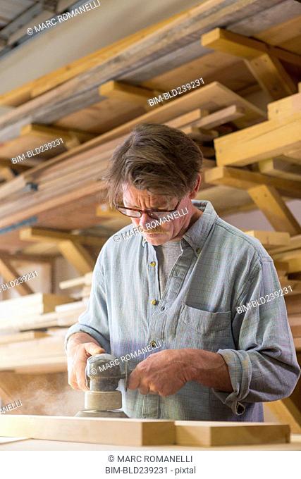 Caucasian carpenter sanding wood in workshop