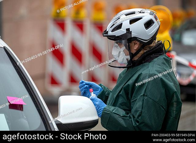 03 April 2020, Bavaria, Nuremberg: An employee of the public health department takes a smear in a corona test centre from a person in his car