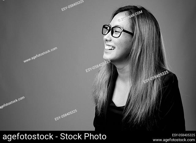 Studio shot of young Asian businesswoman against gray background in black and white