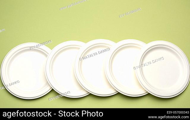 empty white paper disposable plates on a green background, top view. The concept of rejection of plastic, environmental conservation