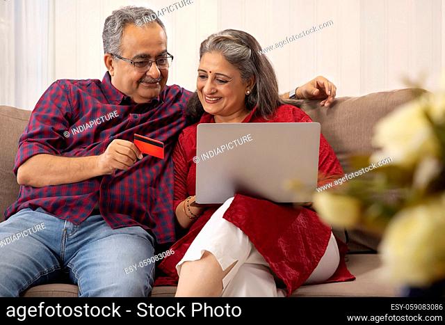 A HAPPY COUPLE SITTING TOGETHER AND DOING ONLINE TRANSACTION
