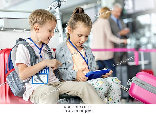 Brother and sister using digital tablet in airport departure area