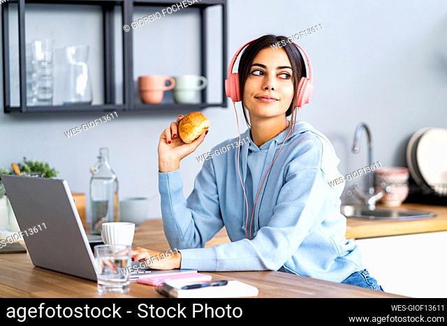 Beautiful woman with laptop having bun in kitchen