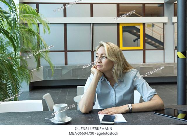 blond woman sits thoughtfully in front of writing pad, looking aside, lost in thought