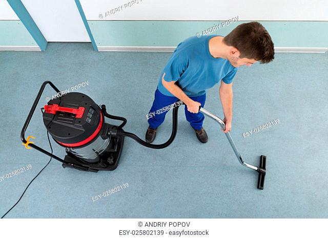 Young Happy Male Worker Cleaning Floor With Vacuum Cleaner