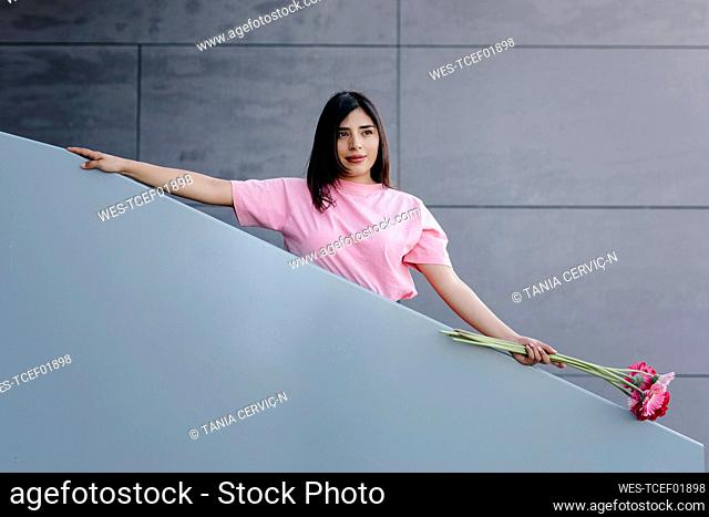 Beautiful woman with flowers standing at railing in front of gray wall