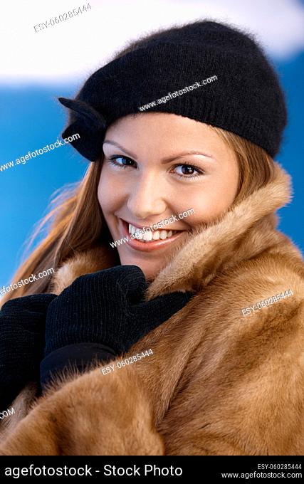 Elegant young woman dressed up warm in fur coat, cap and gloves, enjoying wintertime, smiling