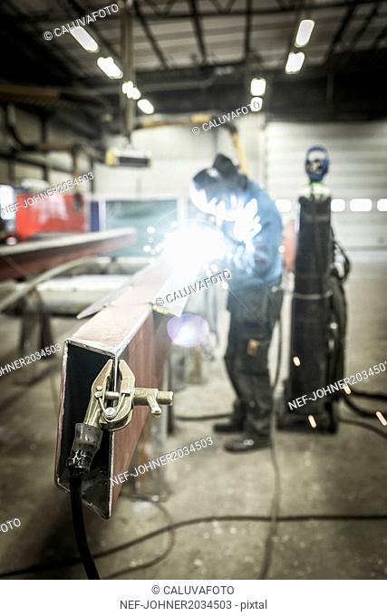 Clamp on metal structure, man welding on background
