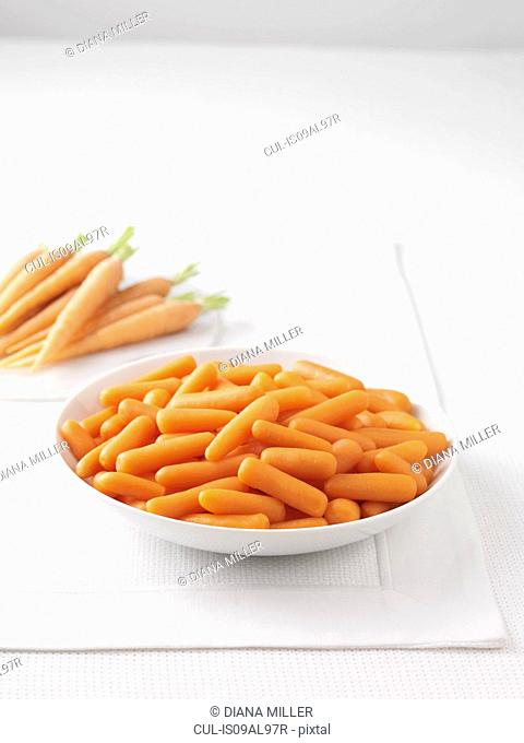 Raw carrots on marble cutting board and bowl of boiled carrots