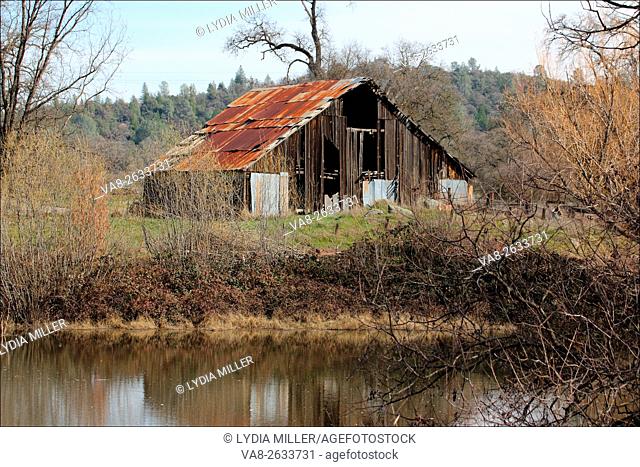 The smooth surface of a pond located in Somerset, California, reflects an old wooden barn that stands near the water, USA