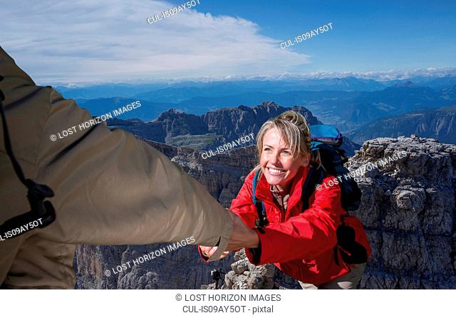 A male climber helping his female partner to reach the top of a mountain, Dolomites, Italy