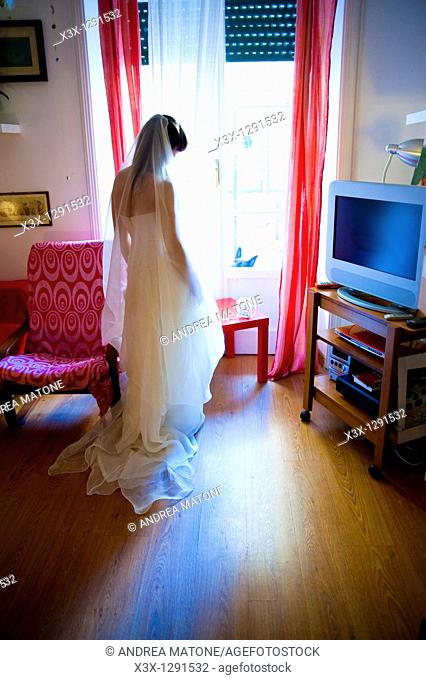 Bride in wedding dress looking out the window door