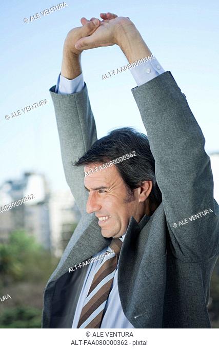 Mature businessman stretching arms outdoors