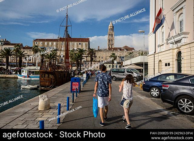 FILED - 27 August 2017, Croatia, Split: Two tourists pass the office of the harbour captain (r) in the harbour. In the background you can see the tower of the...