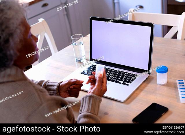 African american woman holding medication container having a video call on laptop with copy space