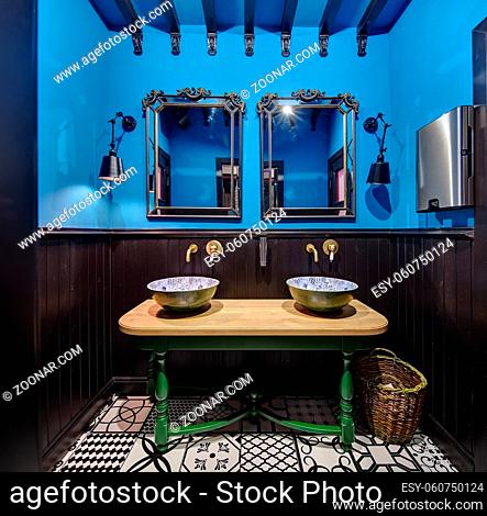 Stylish washroom in a restaurant. Upper part of the walls is blue, and lower part is dark-wooden. On the back wall there are two mirrors