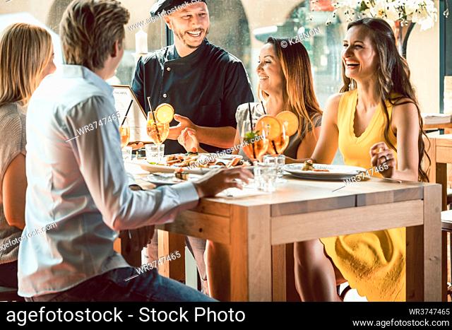 Experienced chef smiling congratulated for the delicious food by four young people at the table of a trendy exclusive restaurant