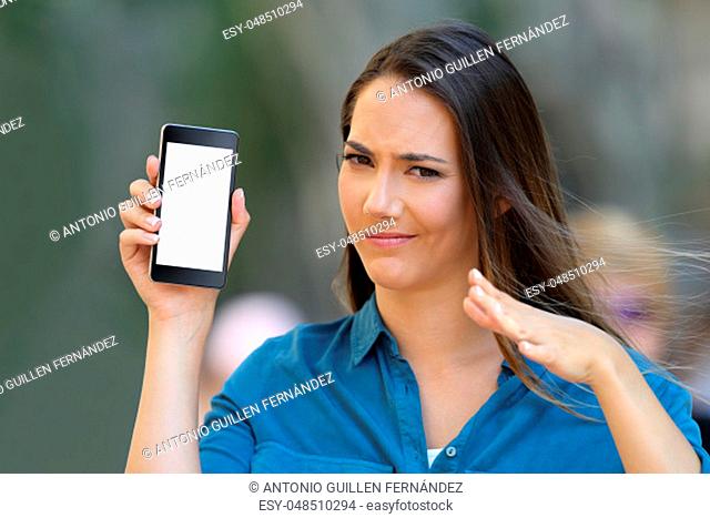 Doubtful woman showing a blank phone screen and looking at camera on the street