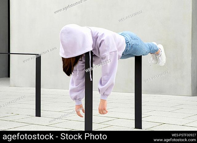 Girl in hooded shirt lying on metal by wall