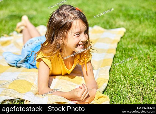 Child lying on the blanket, on the grass in the sun day, little girl take sunbathes on backyard of the house on a sunny summer day, summer time vacation